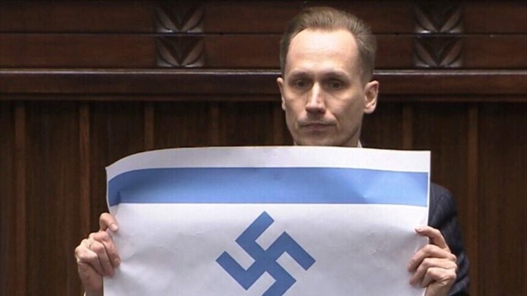 Man in a suit in a courtroom holding a poster with a blue stripe and a large blue swastika symbol.